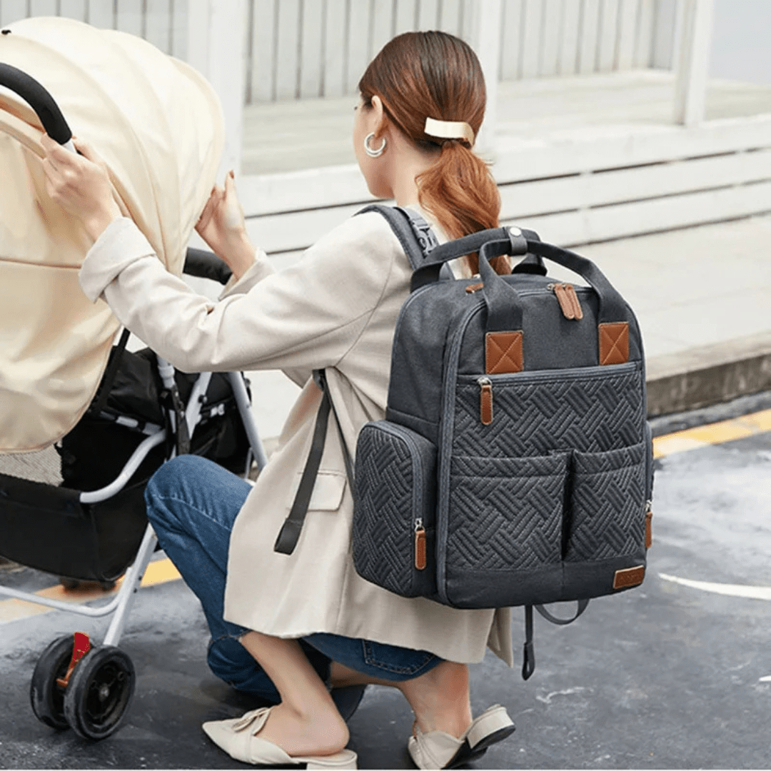 mama schiebt kinderwagen mit grauem wickelrucksack auf dem ruecken