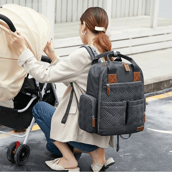 mama schiebt kinderwagen mit grauem wickelrucksack auf dem ruecken