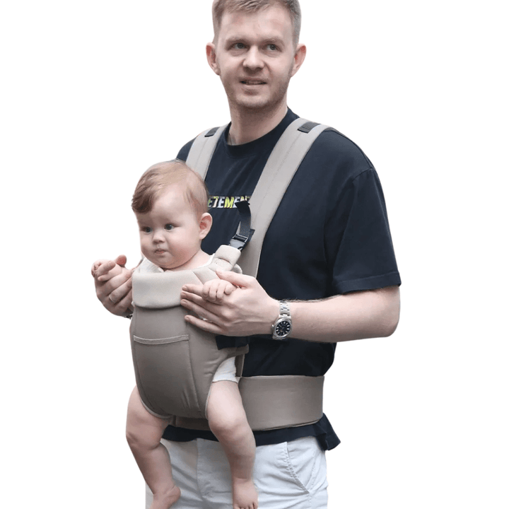 Vater spaziert am Strand mit Baby in der grauen Lacey Babytrage
