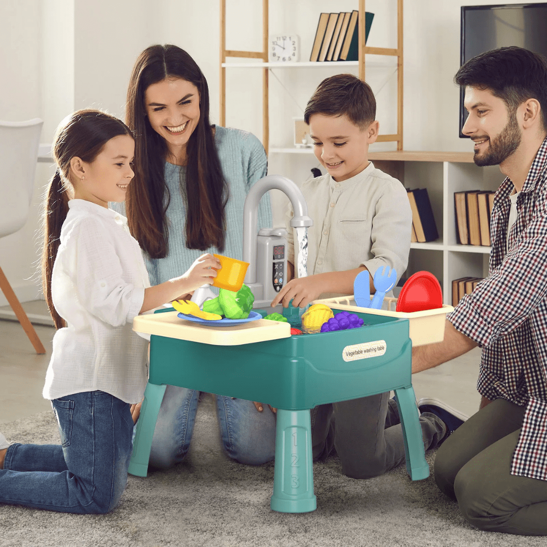 Drei Kinder spielen gemeinsam am SpritzChef, Eltern schauen lachend zu
